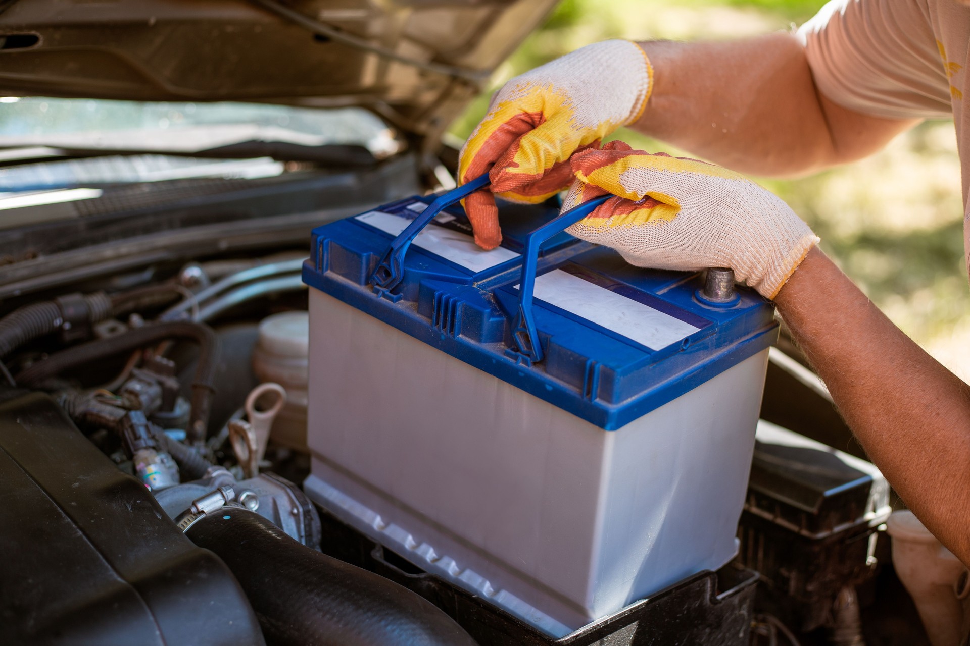 A man removes a battery from under the hood of a car. Battery replacement and repair